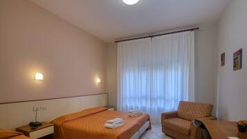 Quarto de hotel com duas camas, uma cadeira, uma escrivaninha e uma janela com cortinas.