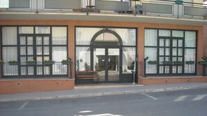 A building with a large arched entrance, a bench outside, and windows with flower boxes. - Albergo La Posta Arezzo (Civitella in Val di Chiana)