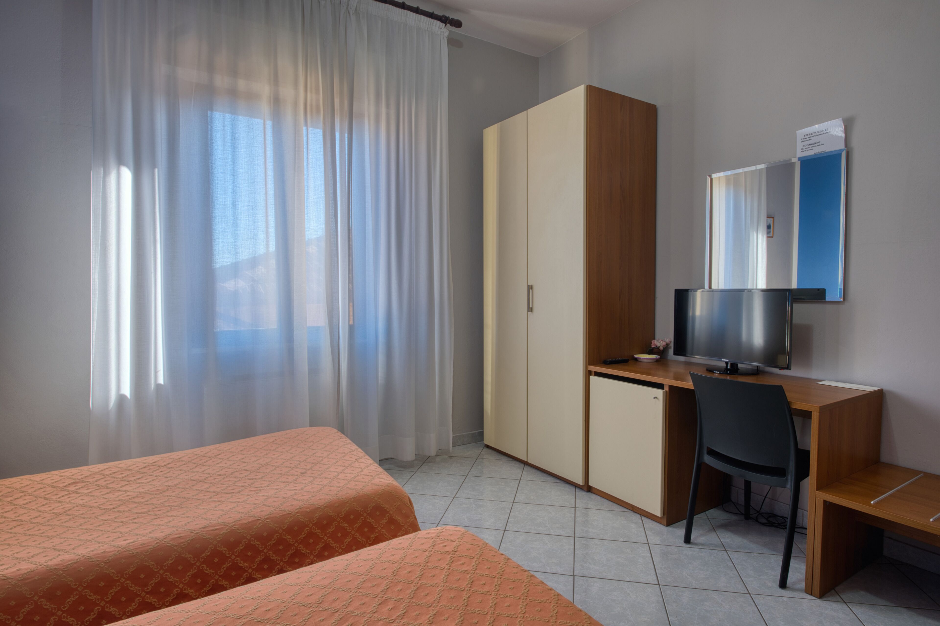 A hotel room with two beds, a desk, a chair, a wardrobe, and a television.