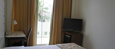 A hotel room with a bed, a desk with a lamp, a television, and a view of the outdoors.