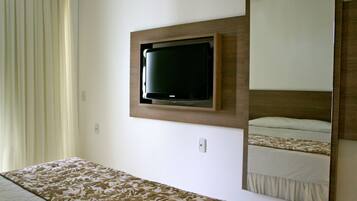 Quarto de hotel com cama, televisão montada e um espelho grande refletindo a cama.