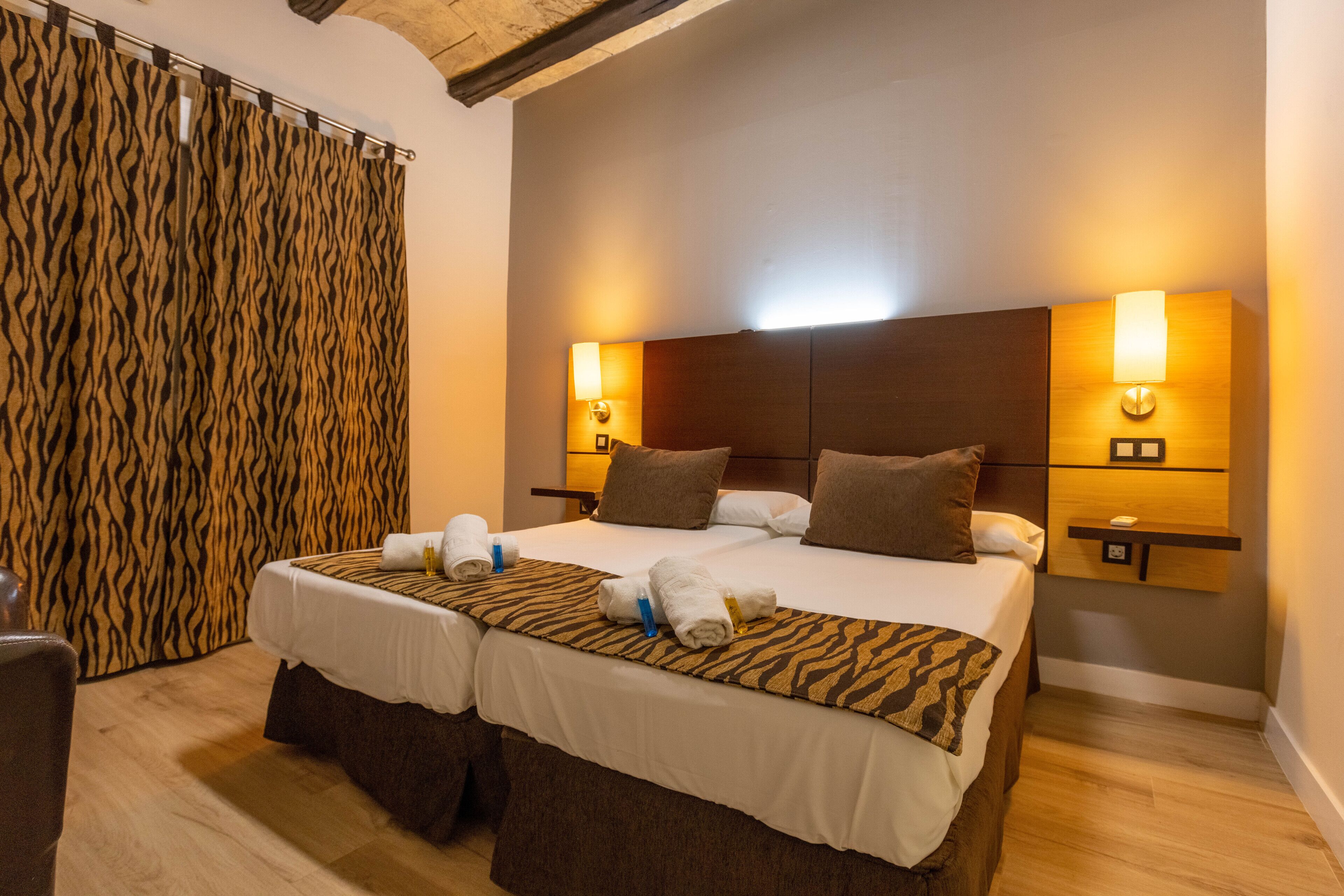 Cama doble con dos almohadas, cabecera, lámparas de noche y cortina con estampado de cebra.