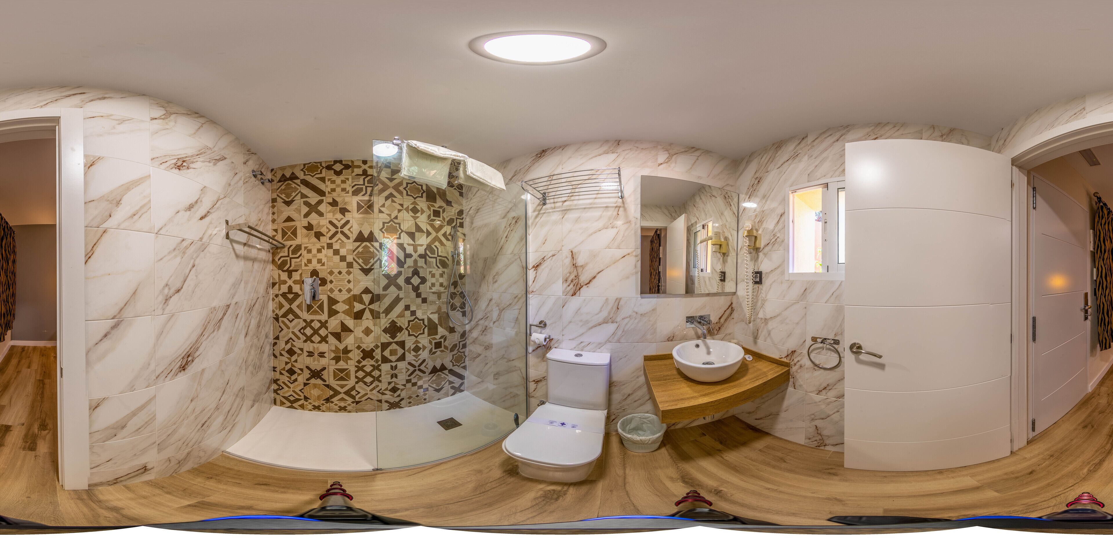 A modern bathroom with a marble wall, a wooden vanity, a toilet, and a shower area.