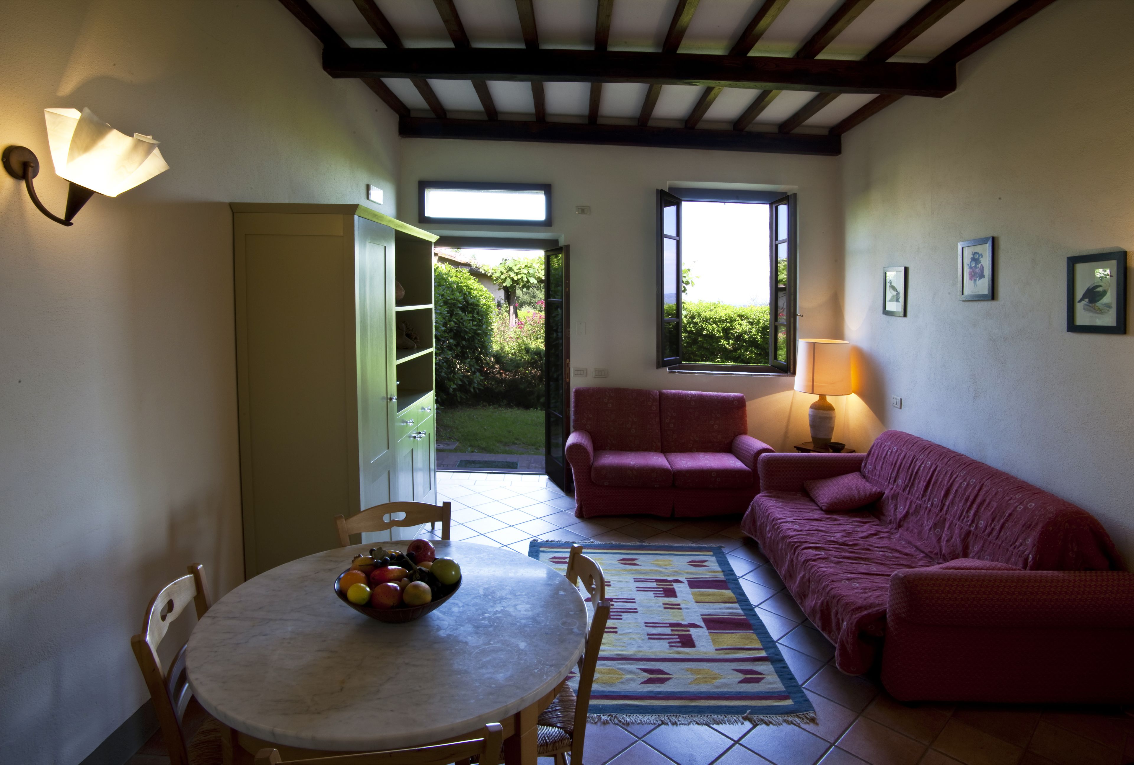 Une pièce comprenant une table à manger, des chaises, un canapé rouge, une lampe et une fenêtre donnant sur un paysage verdoyant.