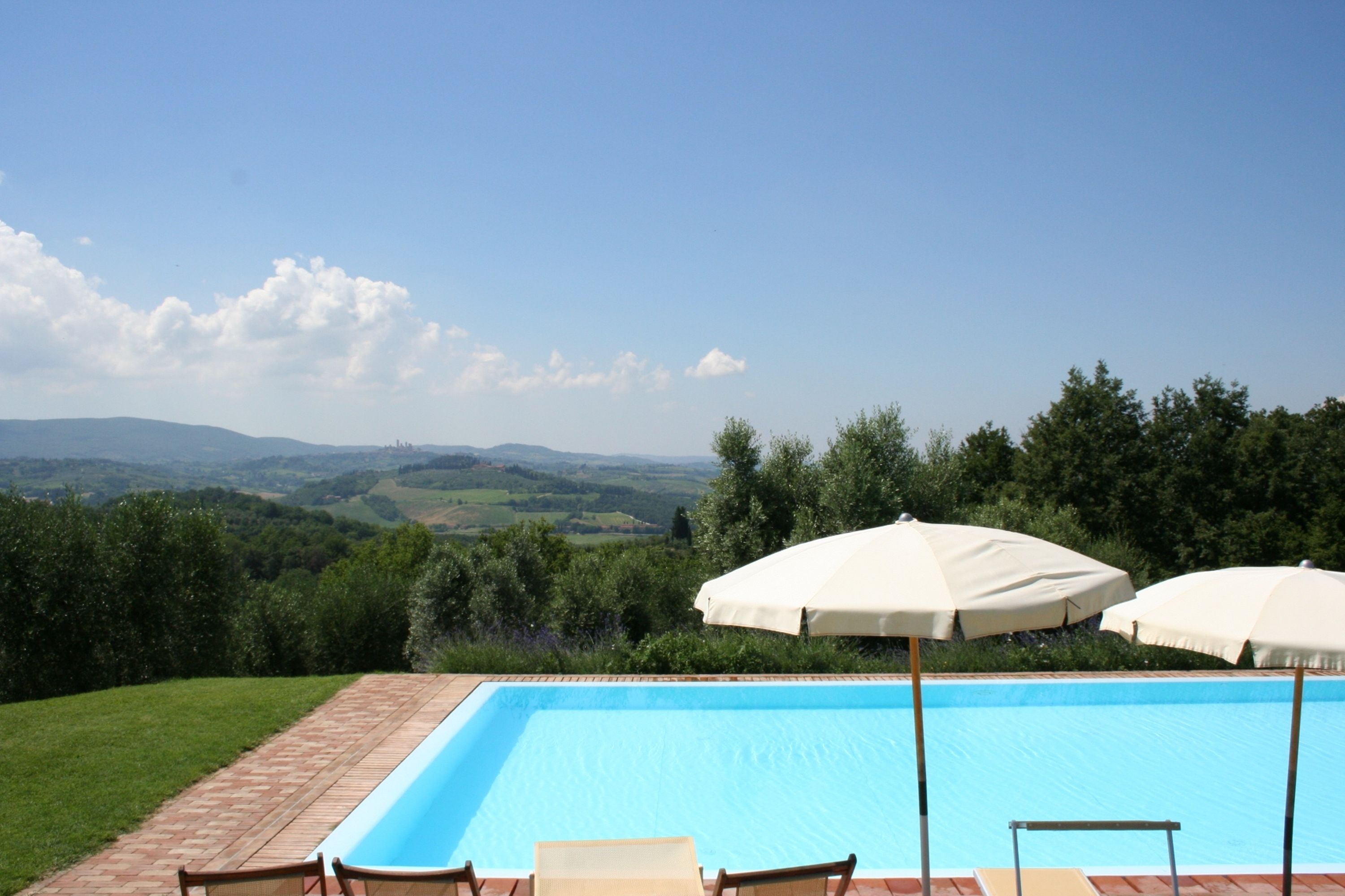 Une piscine avec vue sur la campagne, entourée de verdure et agrémentée de deux parasols.