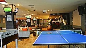 Un espace de loisirs équipé d’un baby-foot, d’une table de ping-pong et de plusieurs écrans diffusant des événements sportifs.
