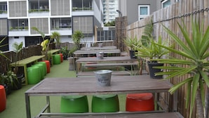 Un espace extérieur aménagé en terrasse, avec des tables et des chaises, entouré d’une clôture en bambou et de plantes en pot.