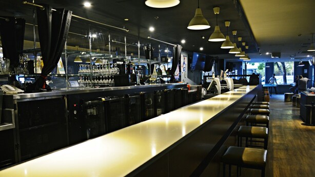 Un espace bar avec un long comptoir, des tabourets et un éclairage suspendu.