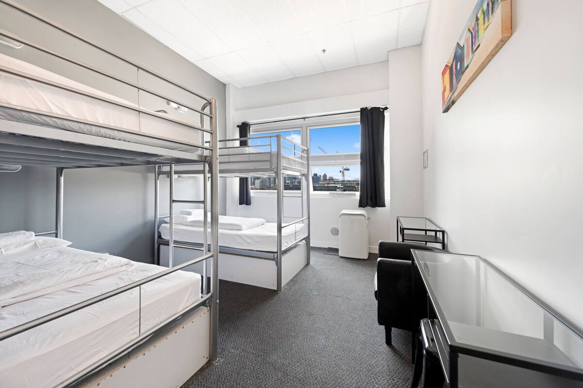 A hotel room with bunk beds, a desk, and a window with a city view.