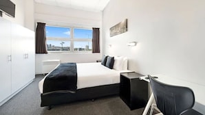 Une chambre d’hôtel avec un lit, un bureau, une chaise, une fenêtre avec des rideaux et une vue sur la ville.