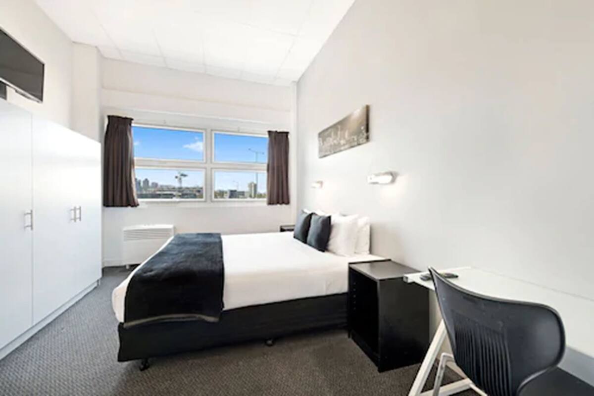 A hotel room with a bed, a desk, a chair, a window with curtains, and a city view.