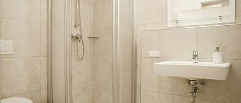 A modern bathroom with a glass-enclosed shower, a white sink, and a toilet.