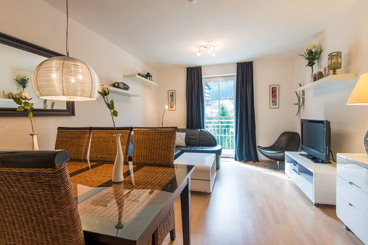 Una sala moderna con comedor, sofá, televisor y balcón con cortinas.