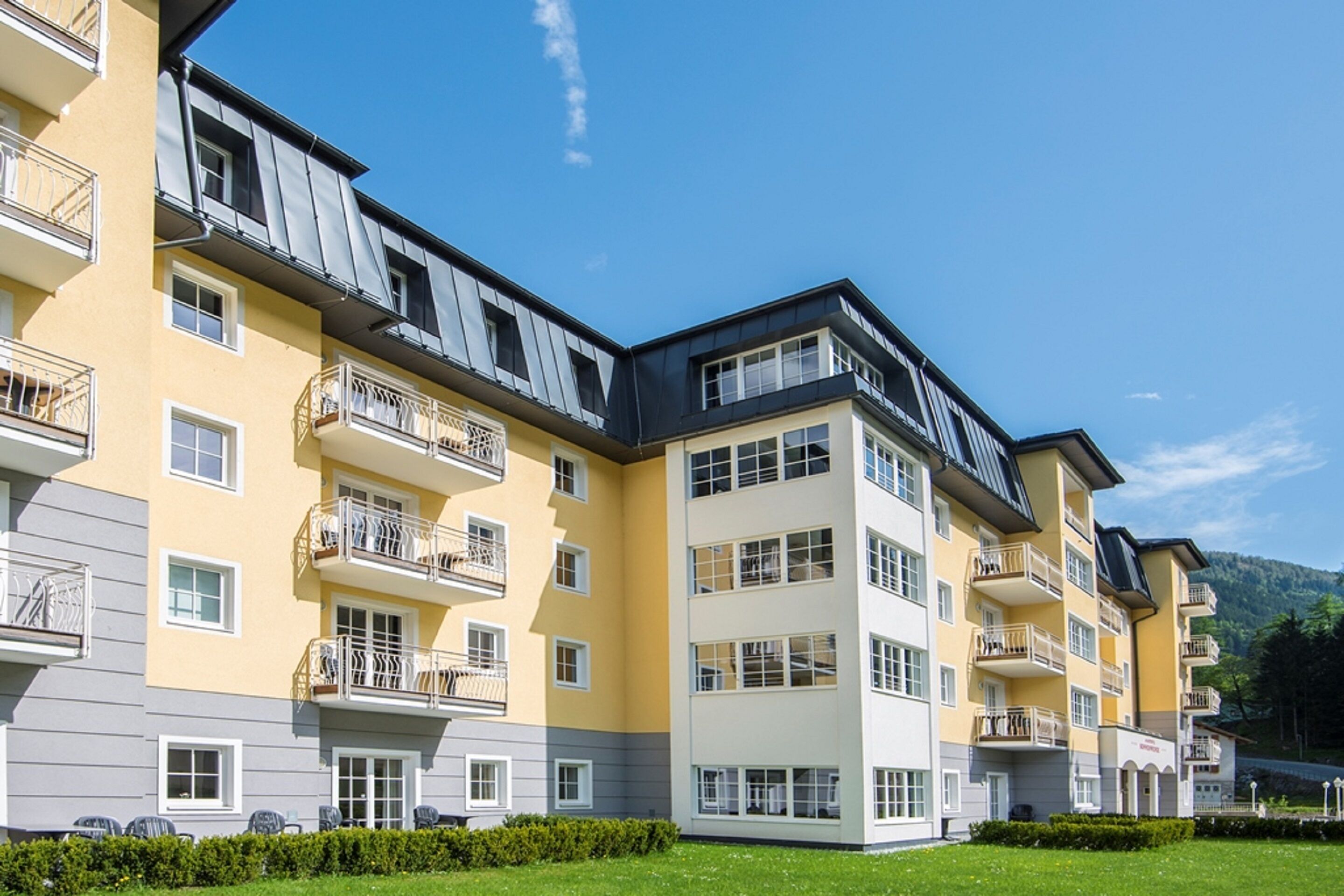 A multi-story hotel with balconies, a flat roof, and a well-maintained lawn.