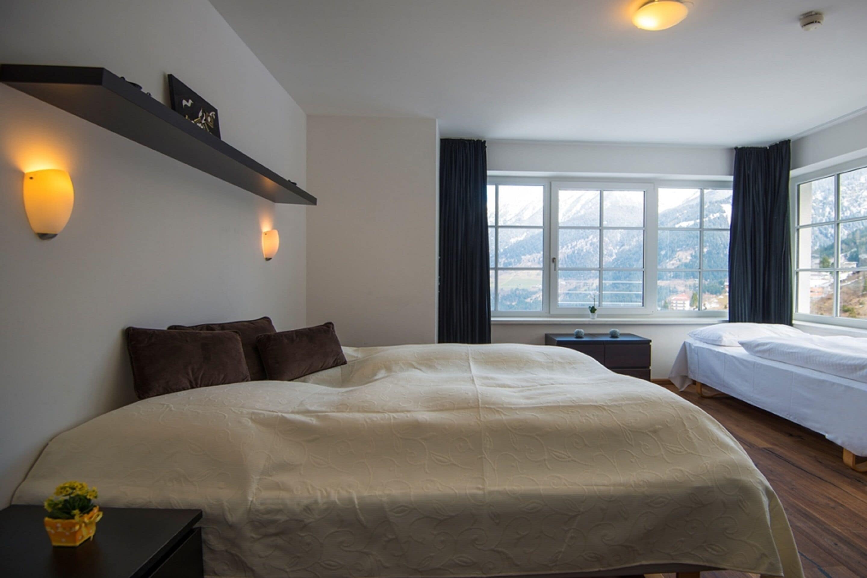 Une chambre avec un grand lit, un plus petit lit, une fenêtre donnant sur la montagne et des lampes fixées au mur.