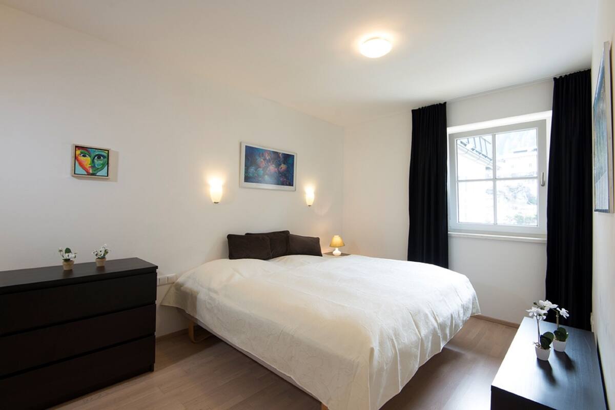 Un dormitorio con cama, cómoda, dos lámparas de pared y dos cuadros.