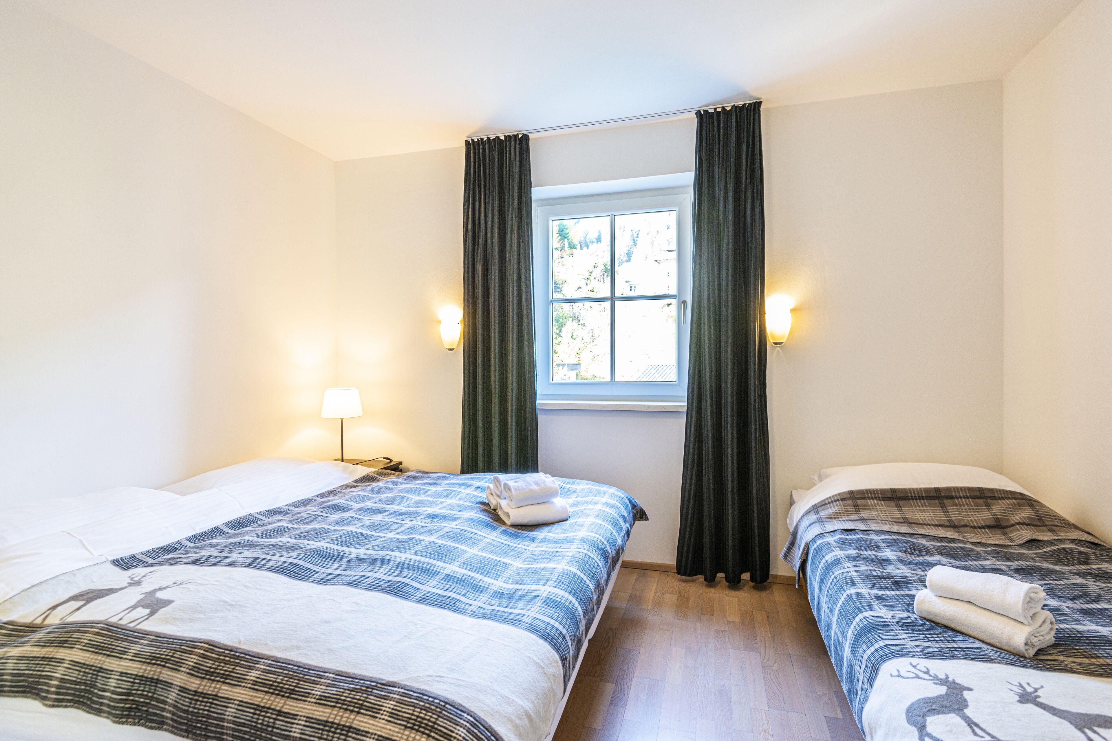 Habitación de hotel con dos camas, ventana con cortinas, lámparas de noche y vistas al exterior.