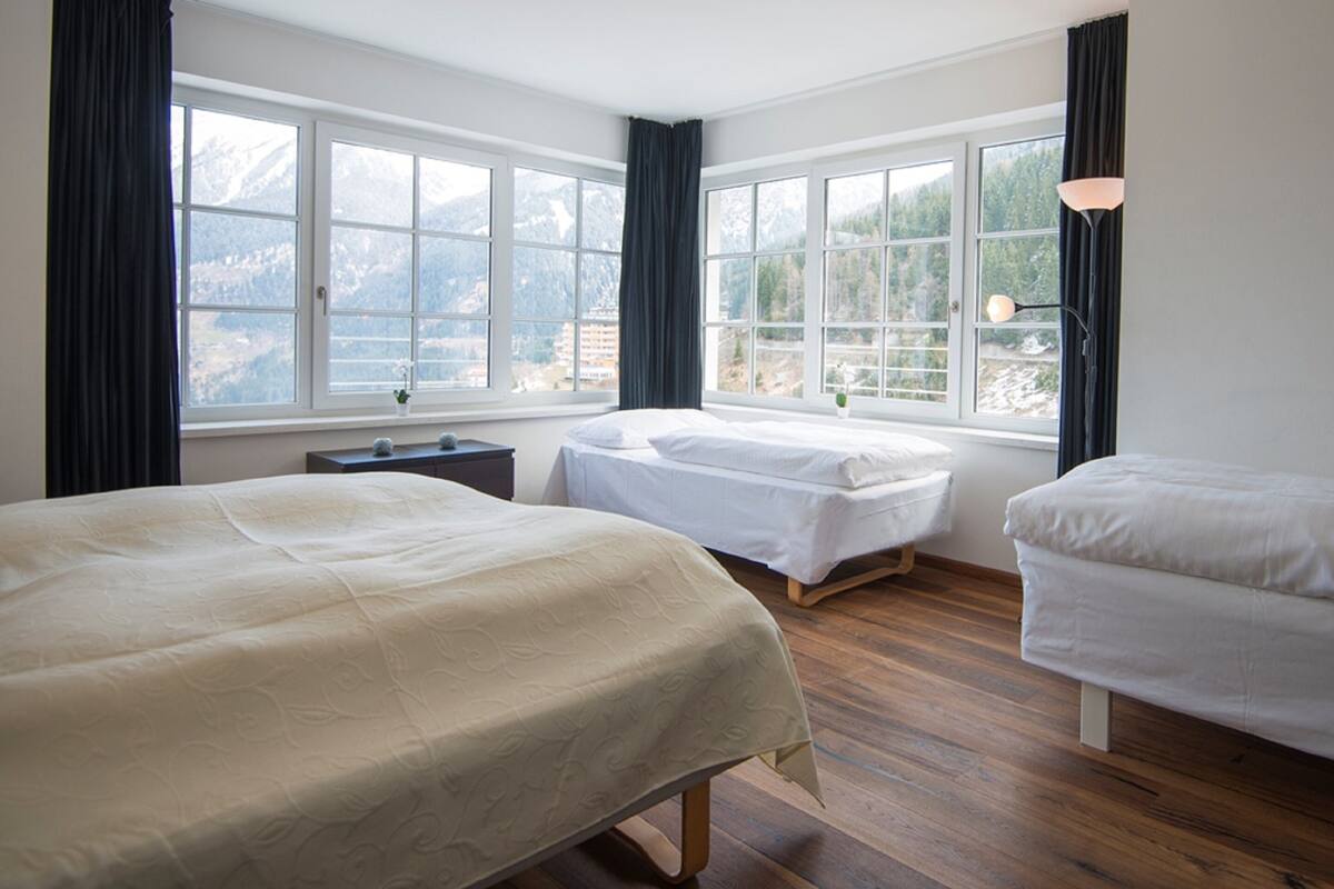 Habitación de hotel con dos camas, una mesita de noche y una ventana con vista a la montaña.