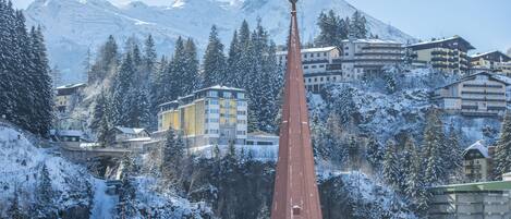 A snow-covered mountain town with a prominent church spire, residential buildings, and a clear view of the mountains in the background.