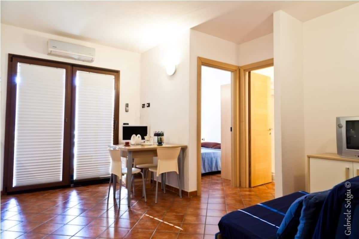 A room with a dining table, chairs, a TV, and a bed.
