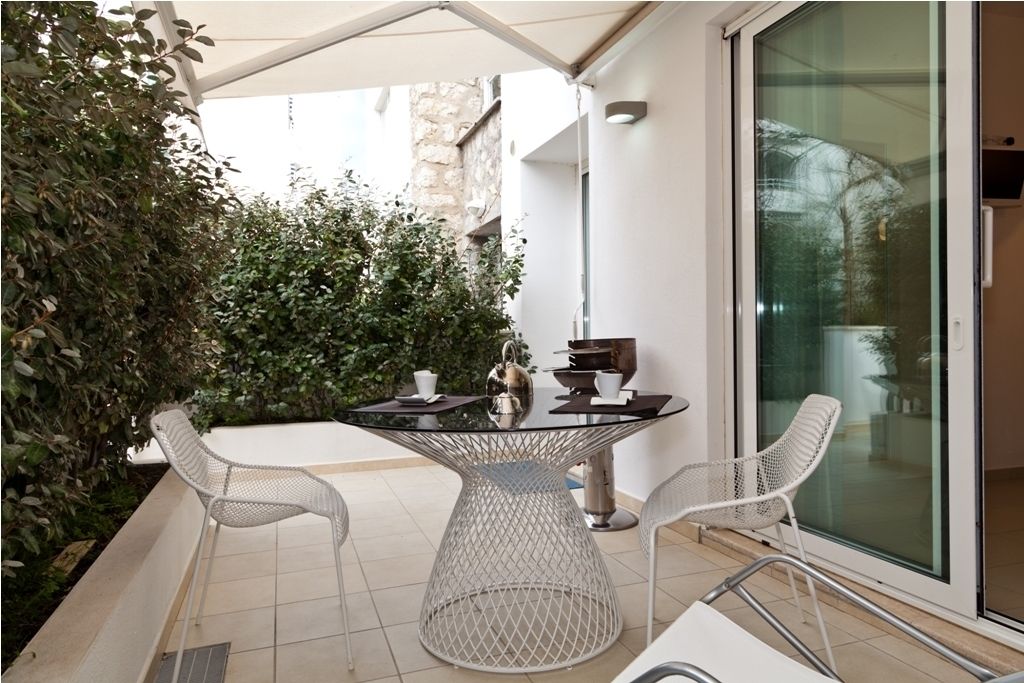 Un patio exterior con una mesa redonda, dos sillas blancas y un ventanal que da a un balcón.