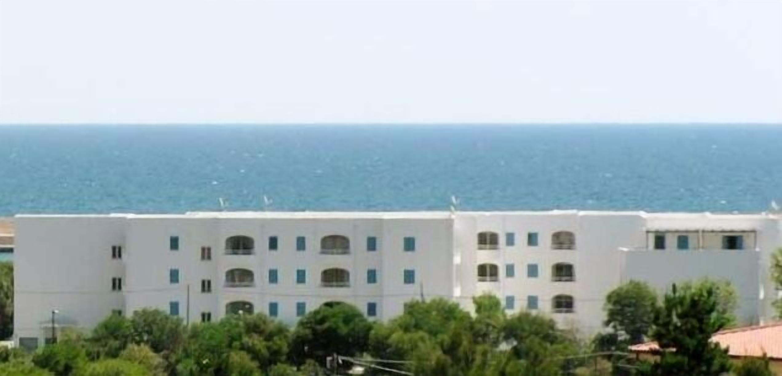 A white multi-story building with a flat roof, located near a body of water.