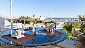 Comedor con una mesa preparada para dos, con vista a un puerto deportivo lleno de barcos y un cielo azul despejado.