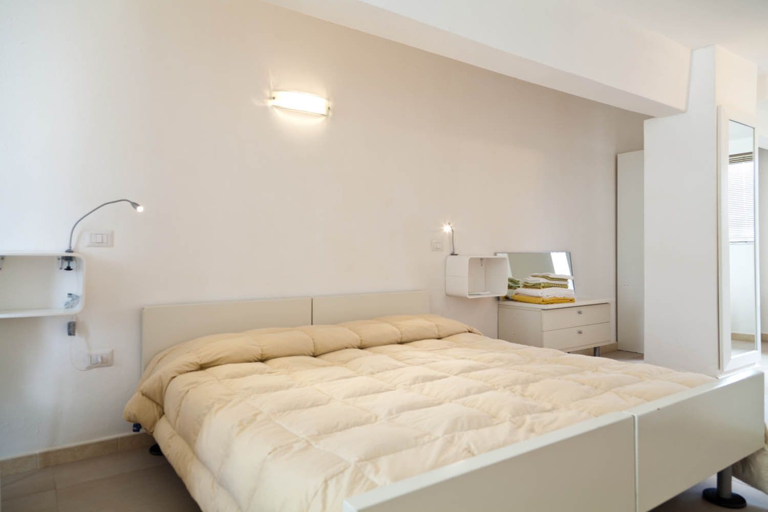 Ein Schlafzimmer mit Bett, Nachttisch, Spiegel und Wandleuchte.