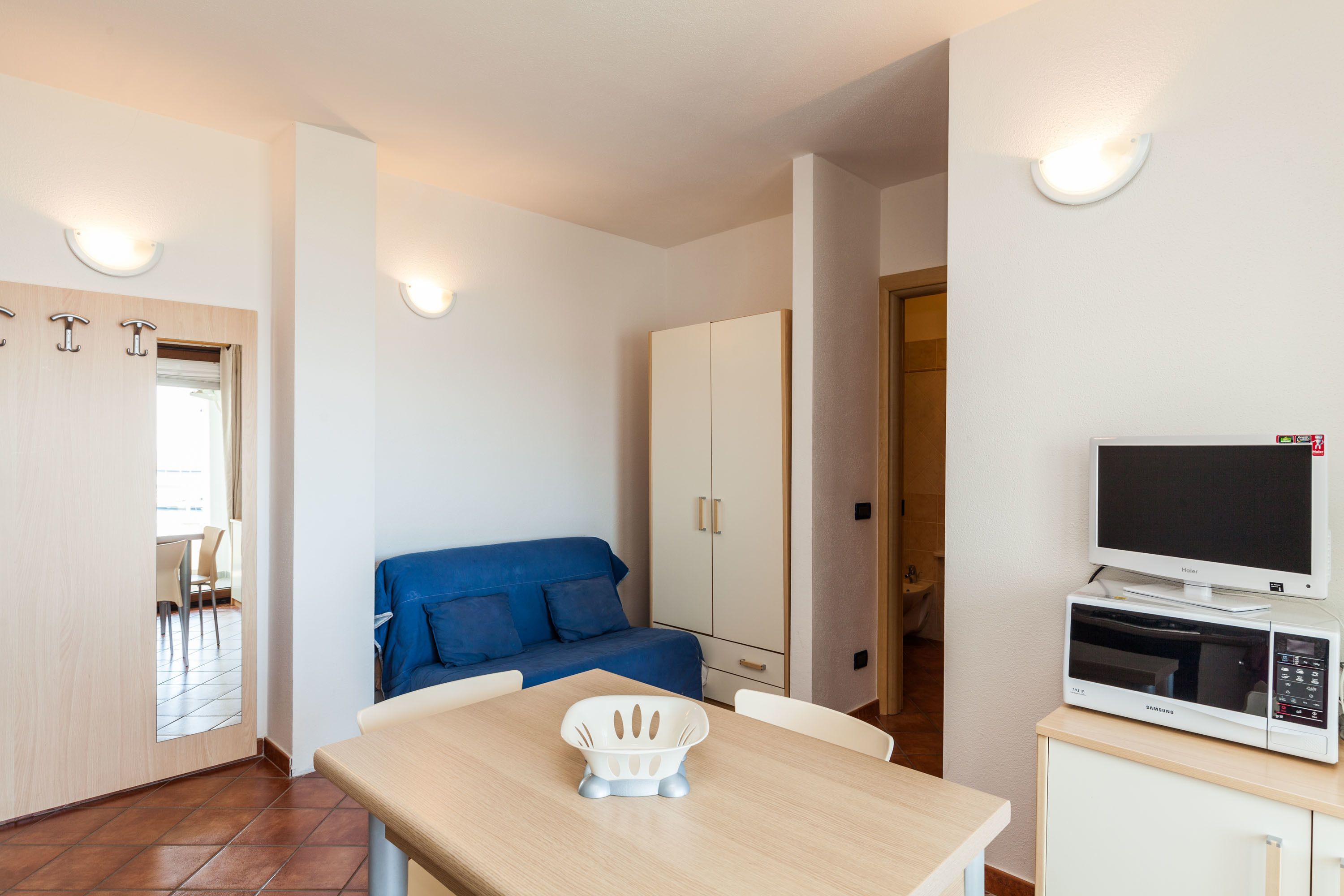 A compact room with a dining table, a blue sofa, a cabinet with a microwave, and a TV.
