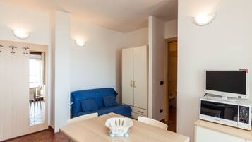 A compact room with a dining table, a blue sofa, a cabinet with a microwave, and a TV.