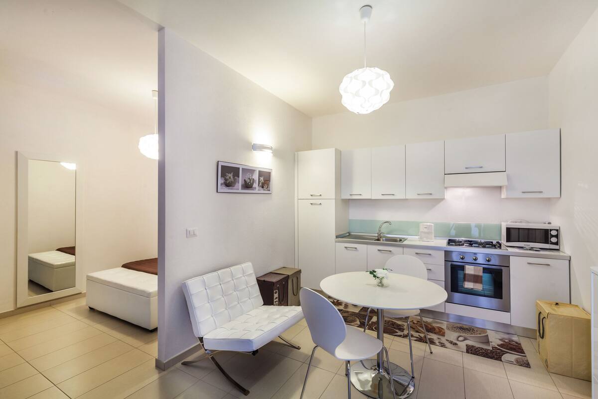 A compact kitchen with white cabinets, a microwave, and a stove. There is a dining area with a white table and chairs.