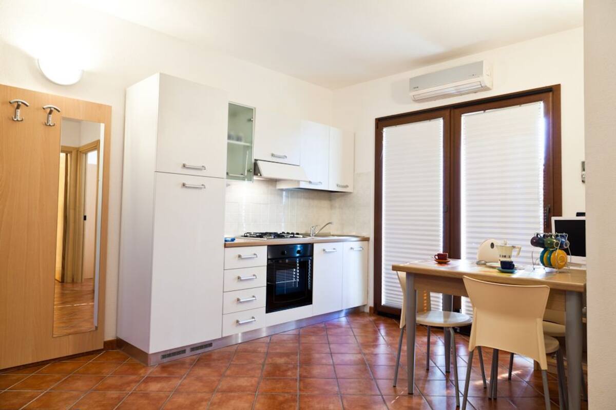 A compact kitchen with white cabinets, a stove, and a dining area with a table and chairs.