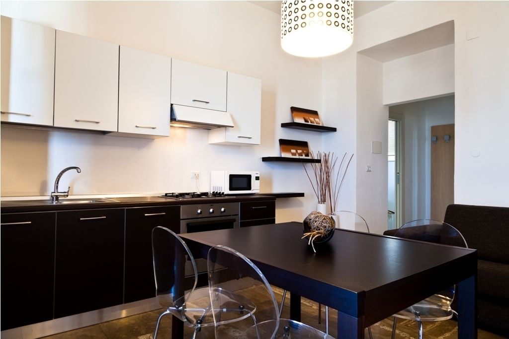 Une cuisine moderne avec des meubles de couleur sombre, un îlot central et un coin repas doté de chaises transparentes.