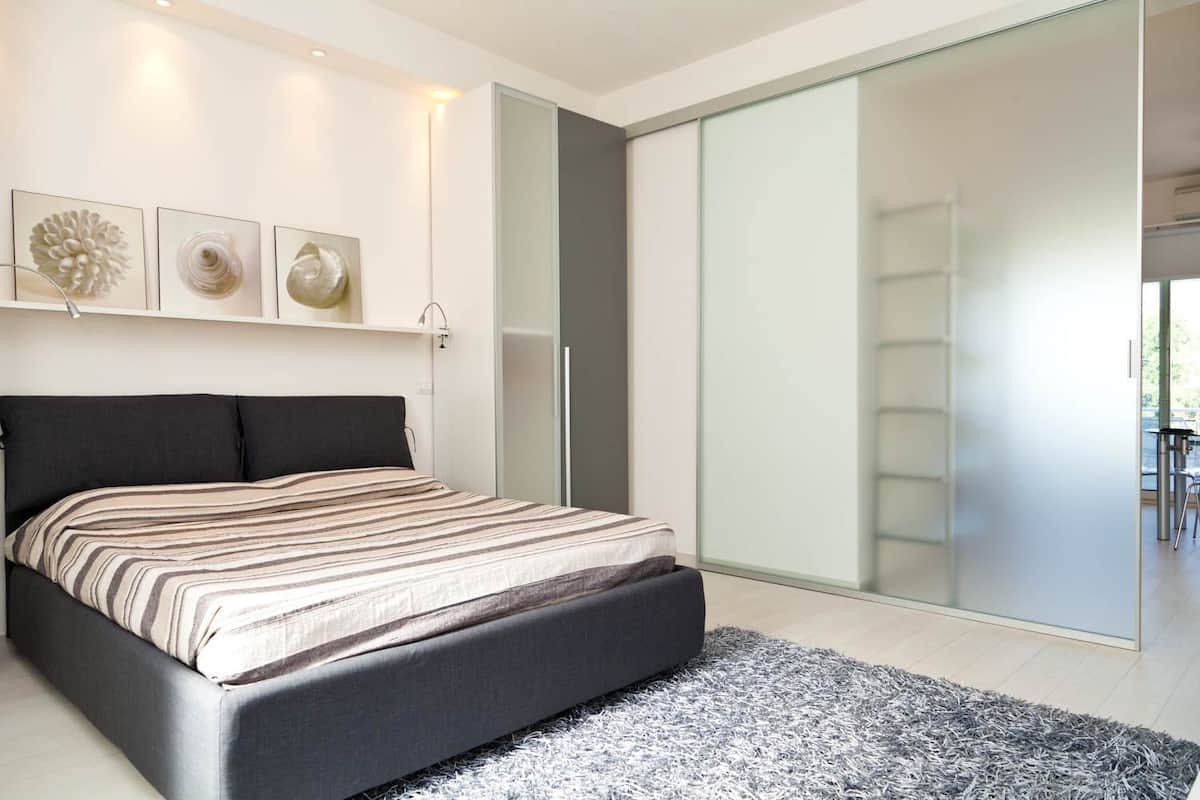 A modern bedroom with a large bed, a glass sliding door closet, and three wall-mounted artworks.