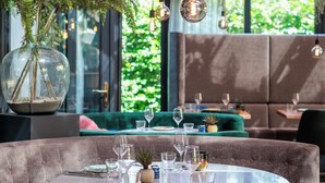A restaurant with a round table set for dining, hanging plants, and a modern interior design. - Paviljoen Hotel (Rhenen)
