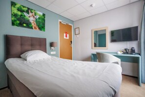 A hotel room with a bed, a desk, a chair, a television, and a door. - Paviljoen Hotel (Rhenen)