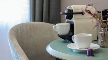 A room with a table set for two, a coffee machine, a cup, a saucer, and a vase with flowers.