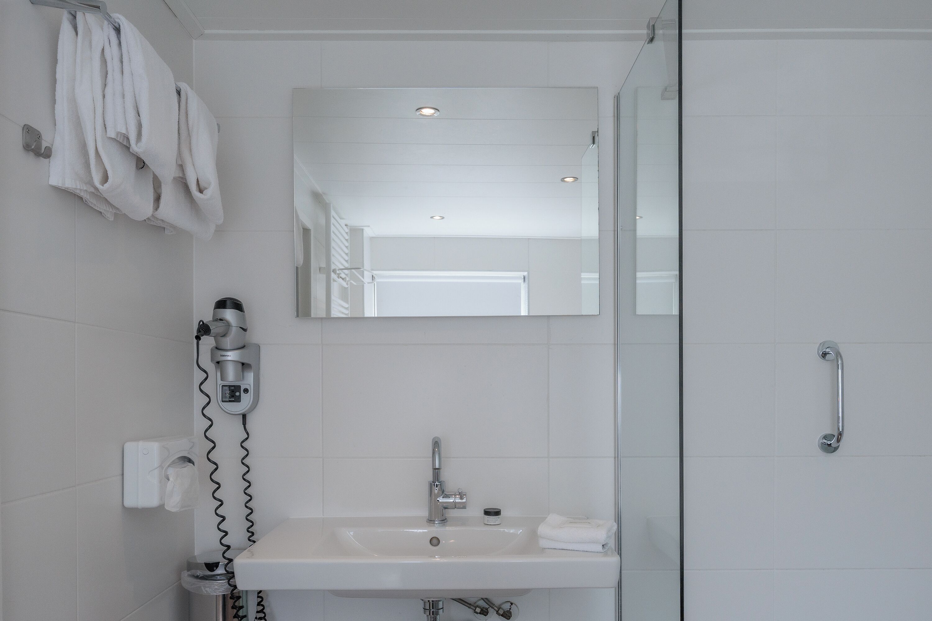 A bathroom with a white sink, a mirror, a towel rack, and a shower area.