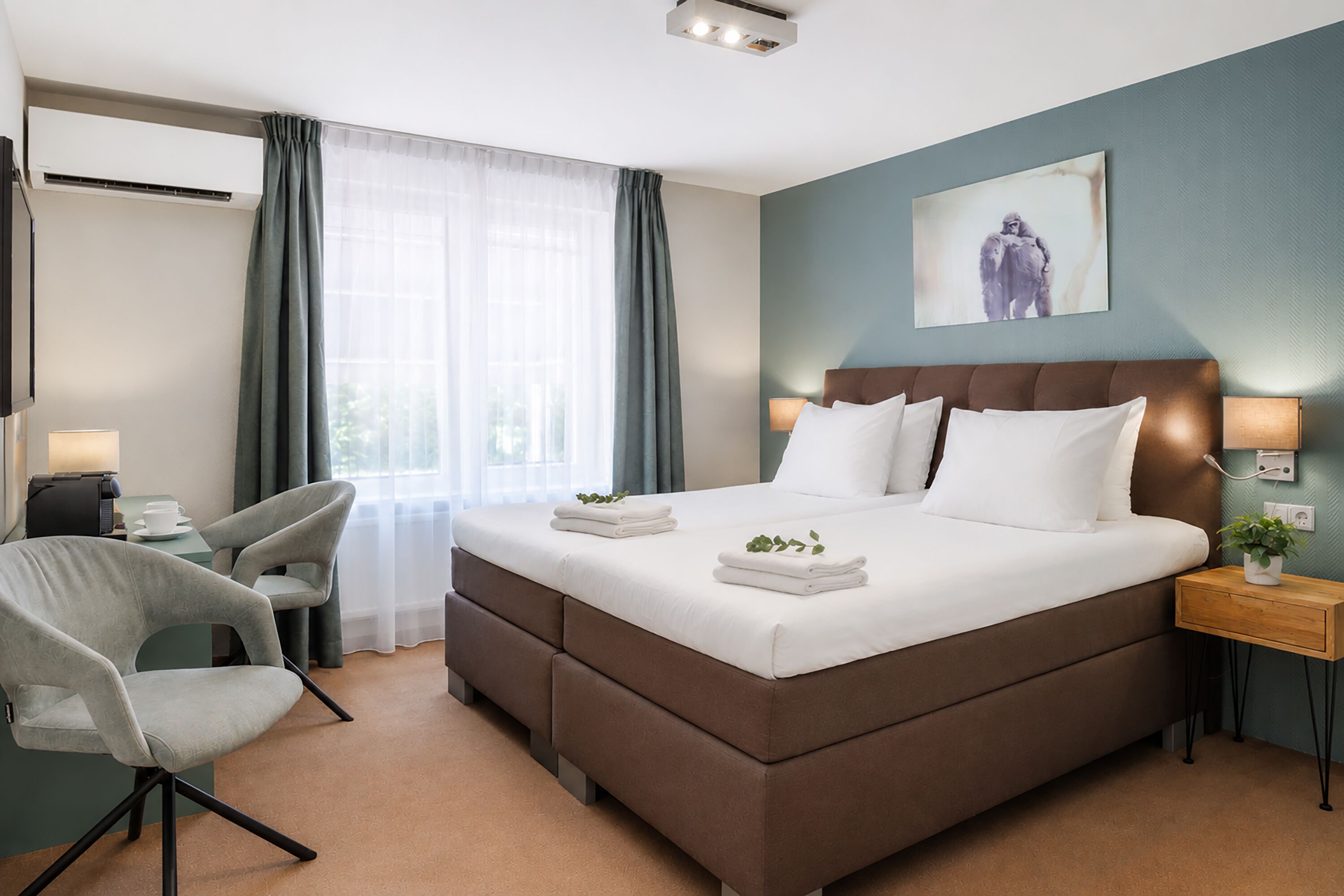 Habitación de hotel con cama, escritorio, silla, mesita de noche y aire acondicionado instalado en la pared.