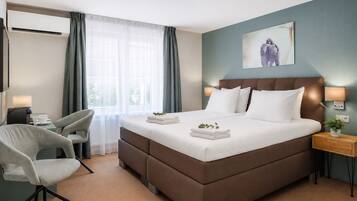 Habitación de hotel con cama, escritorio, silla, mesita de noche y aire acondicionado instalado en la pared.