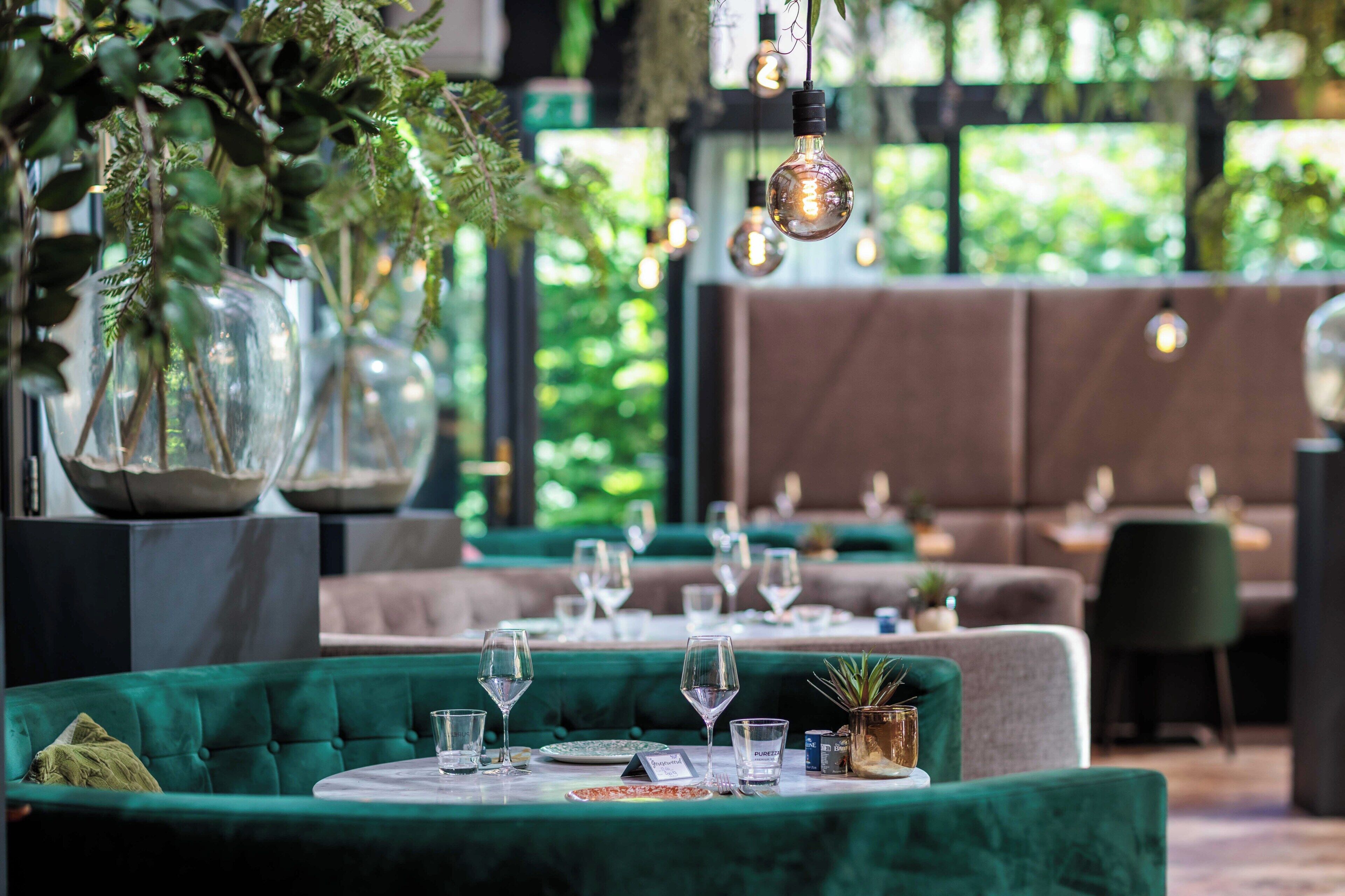 A restaurant with round tables, green upholstered seating, and hanging light fixtures.
