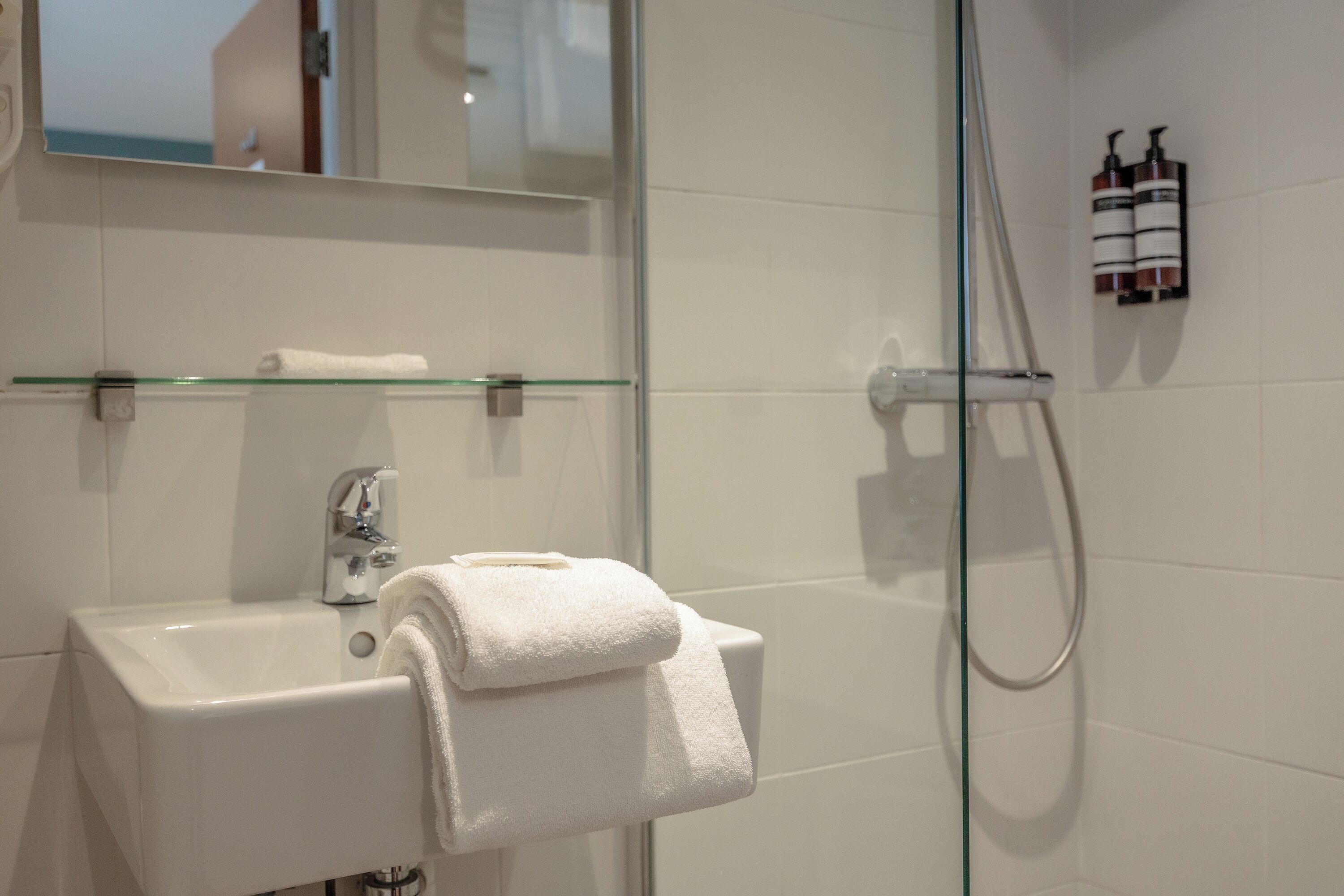 A bathroom with a glass shower enclosure, a white sink, and a towel rack.
