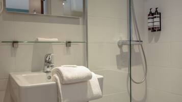 A bathroom with a glass shower enclosure, a white sink, and a towel rack.