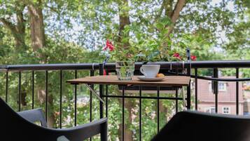 Un balcón con mesa, sillas, una planta en maceta, una copa y una taza.