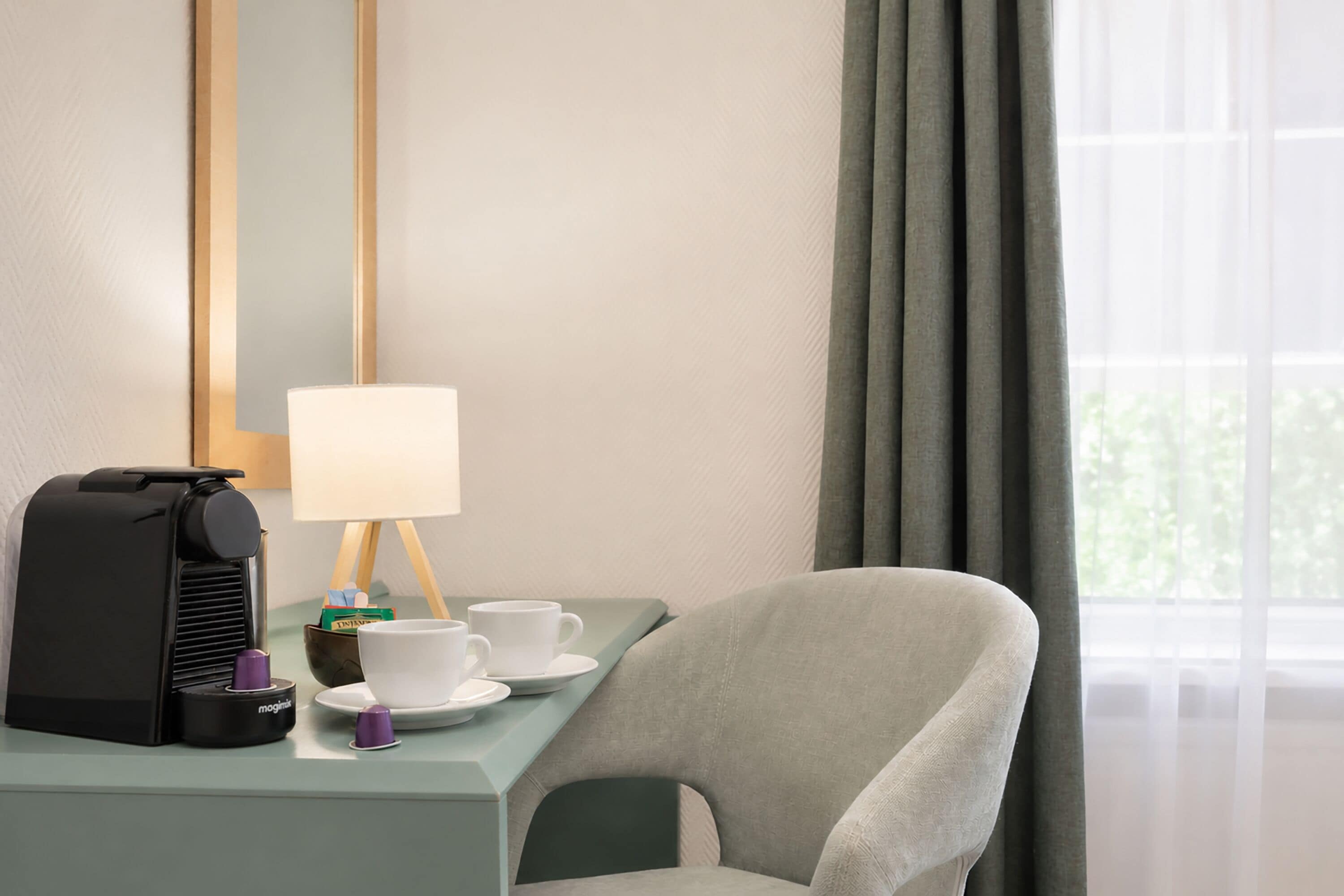 Una camera d'albergo con una macchina per il caffè, tazze, una lampada e una sedia.