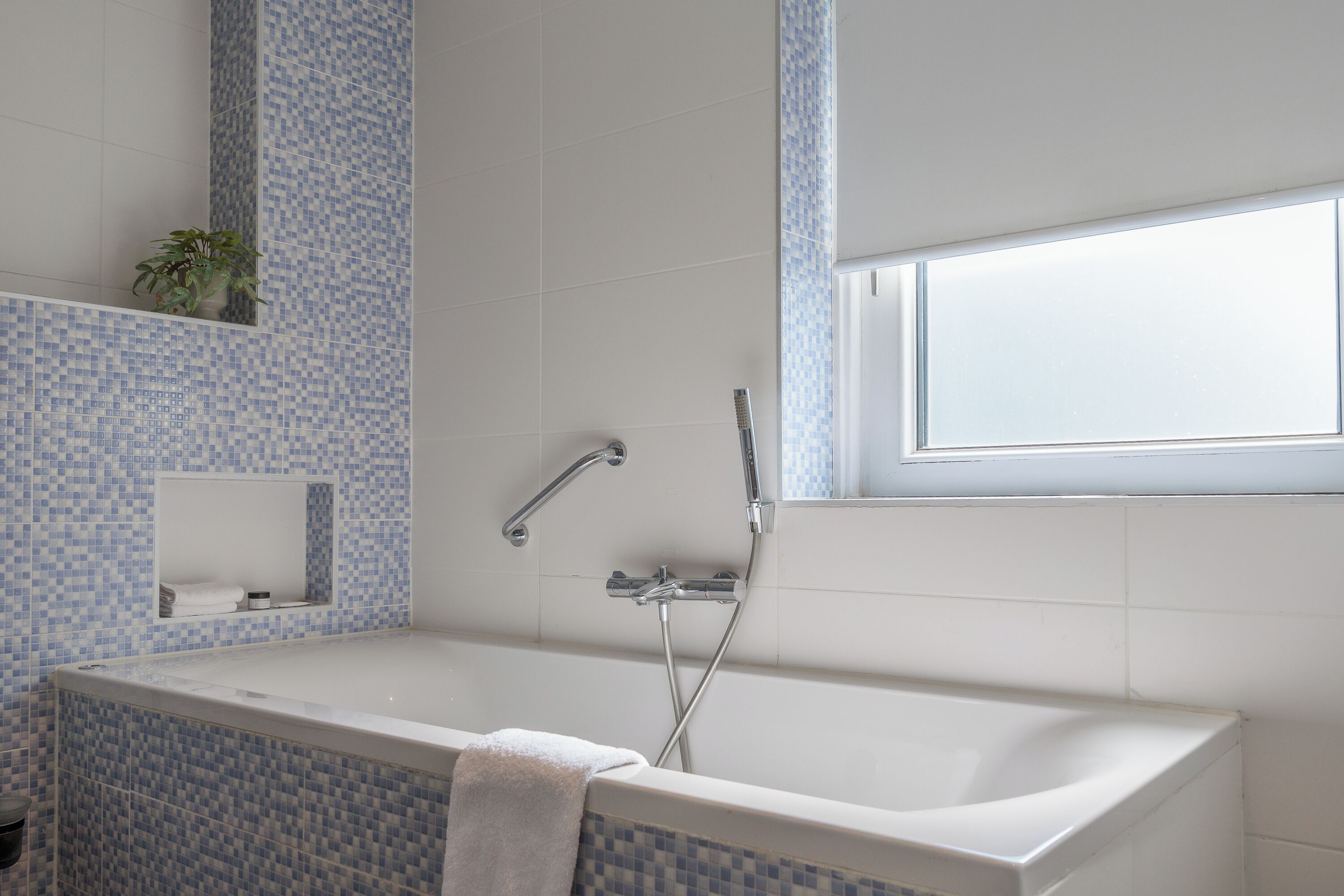 Un baño moderno con bañera, ducha, ventana y planta.