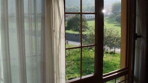 A window with a view of a green landscape and a building in the distance. - Hotel Pugide (Llanes)