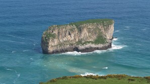 A large, isolated rock formation surrounded by clear blue water. - Hotel Pugide (Llanes)