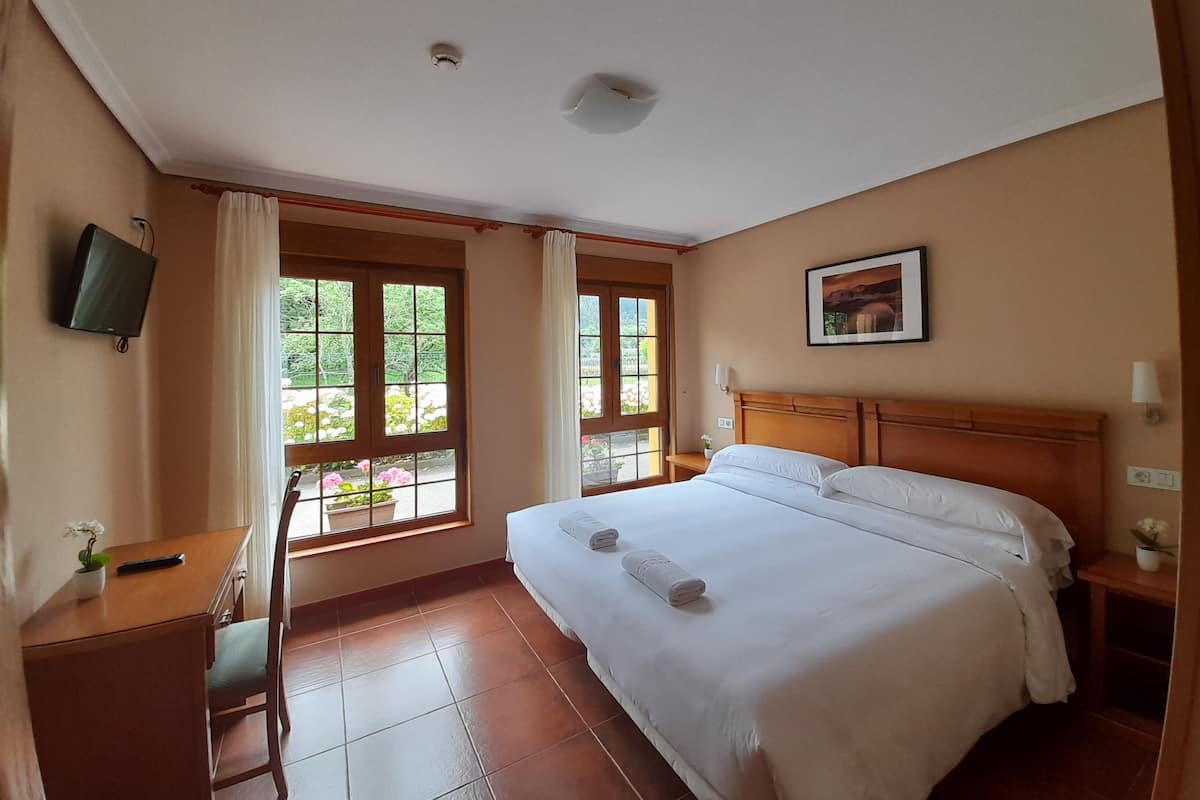 A hotel room with a bed, a desk, a chair, a TV, and windows with curtains.