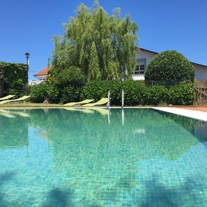 A clear swimming pool with tiled edges, surrounded by lush greenery and a white building with a red roof. - La Regalina (Valdes)